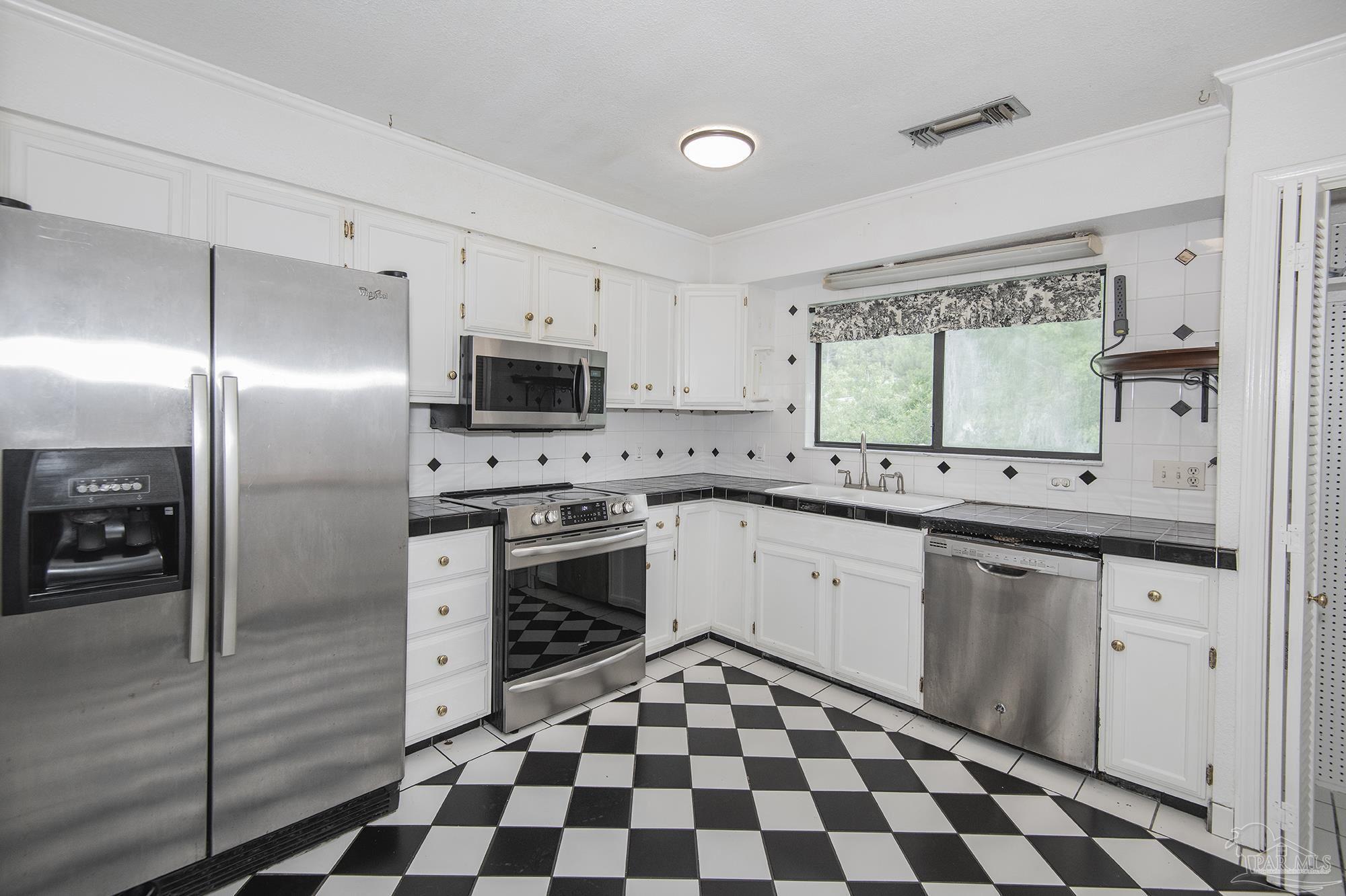 Kitchen with white cabinetry, stainless steel appliances, and black-and-white diamond-pattern tile floors.
