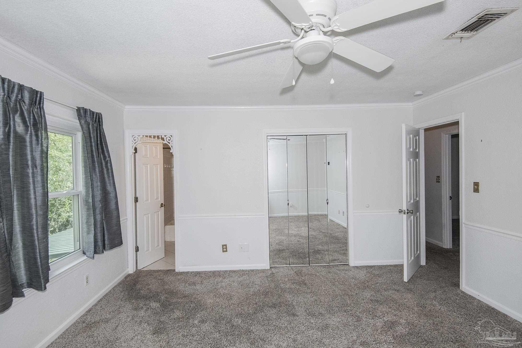 Unfurnished bedroom with mirrored closet doors, gray carpet, and a ceiling fan.
