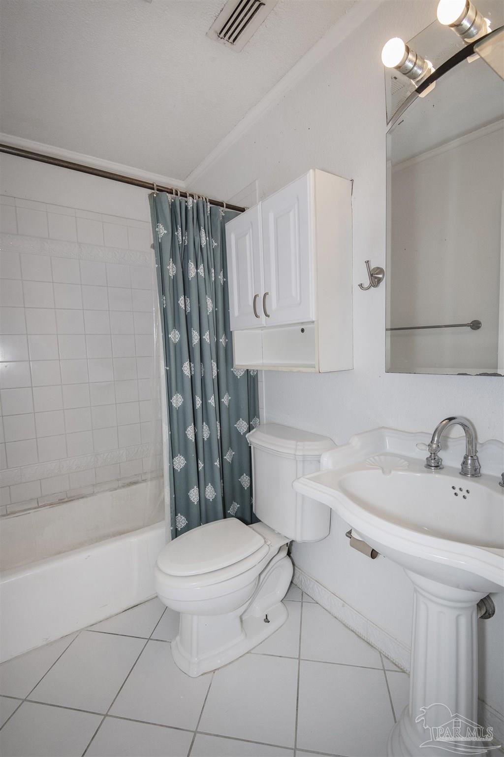 Bathroom with a tiled tub, teal patterned shower curtain, toilet, and pedestal sink.