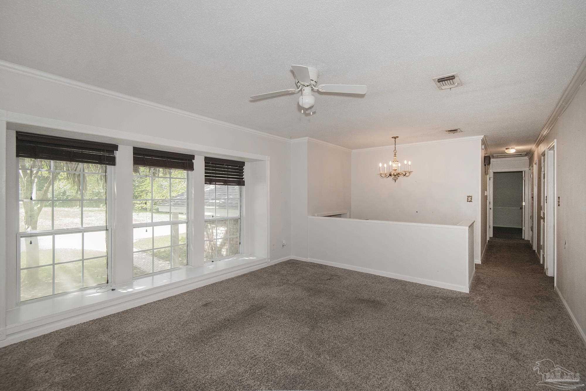 Vacant living and dining area with wide windows, dark blinds, and a chandelier.