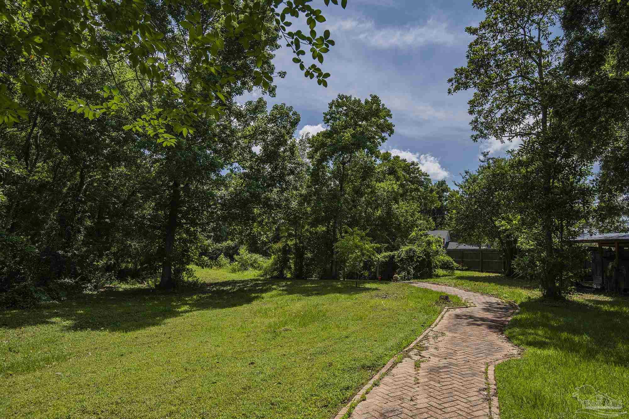 Tree-shaded backyard with a broad lawn and a curving brick walkway.