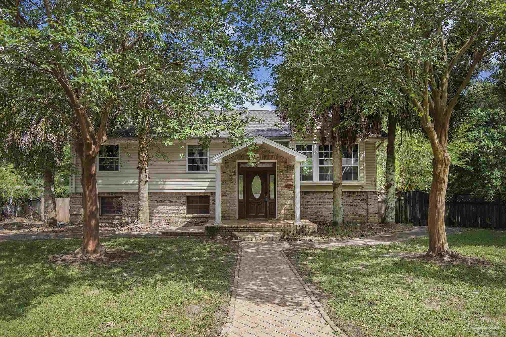 Two-story house with a brick-and-siding exterior, covered entry, and shaded walkway through mature trees.