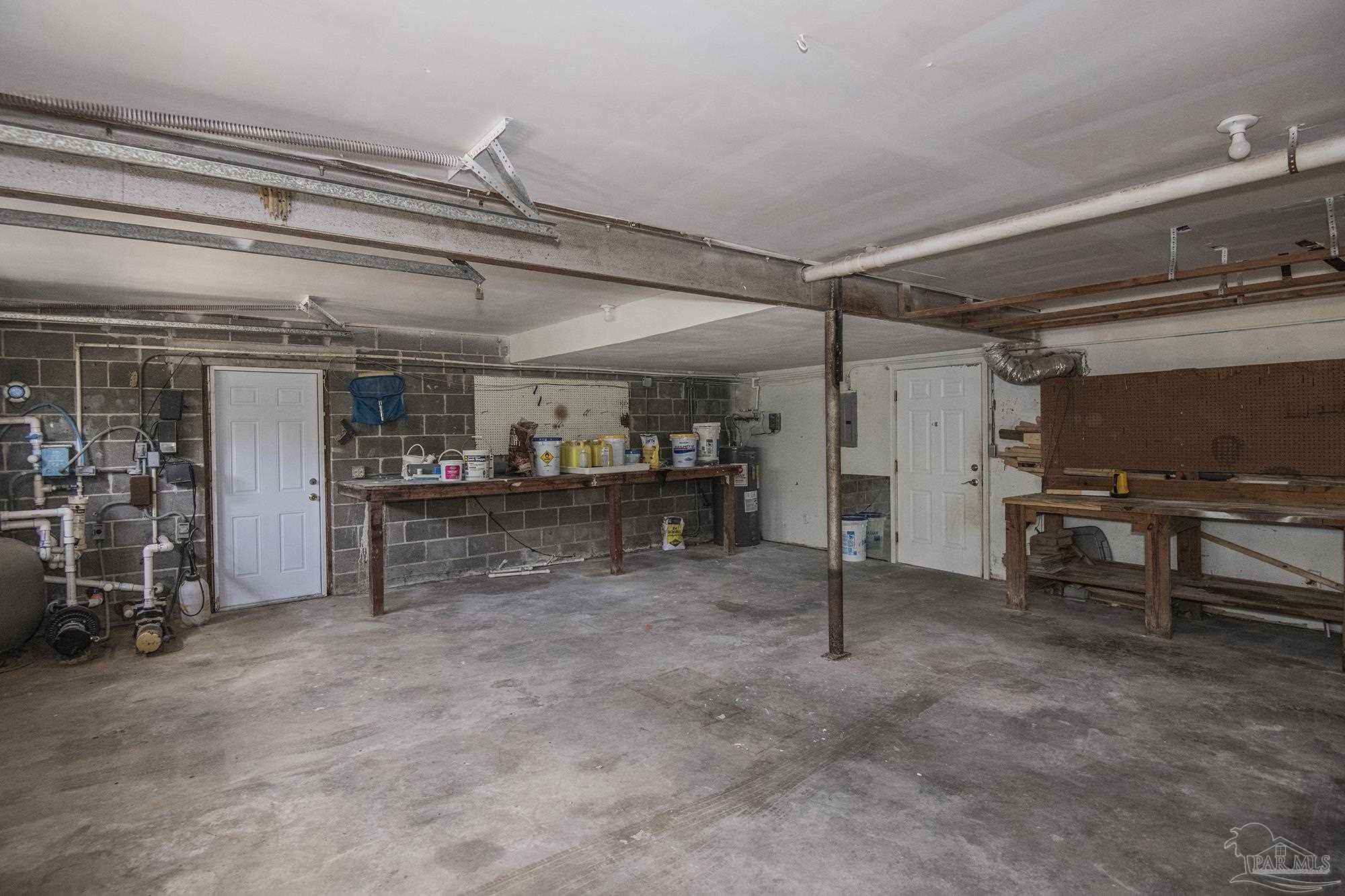 Garage with concrete floor, utility equipment, and wooden workbenches along the walls.