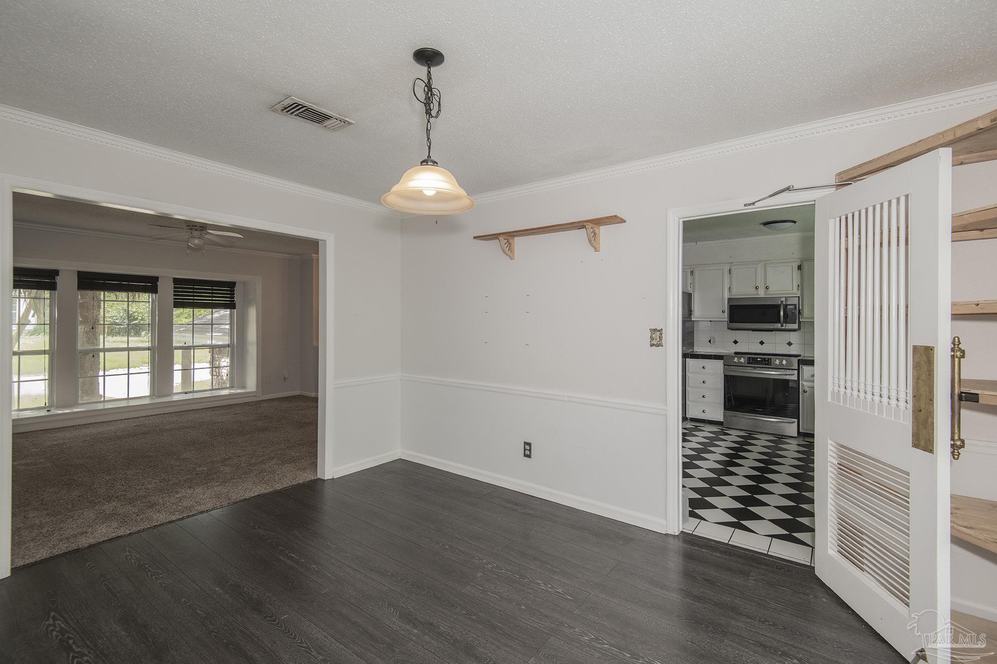 Empty dining area with dark flooring, opening to a carpeted living room and checkerboard-tile kitchen.