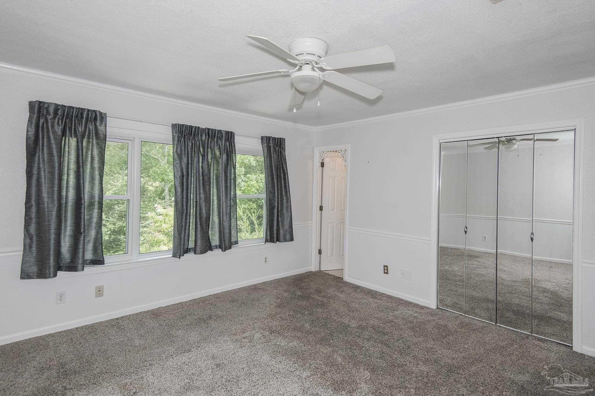 Empty bedroom with gray carpet, curtained windows, a ceiling fan, and mirrored closet doors.