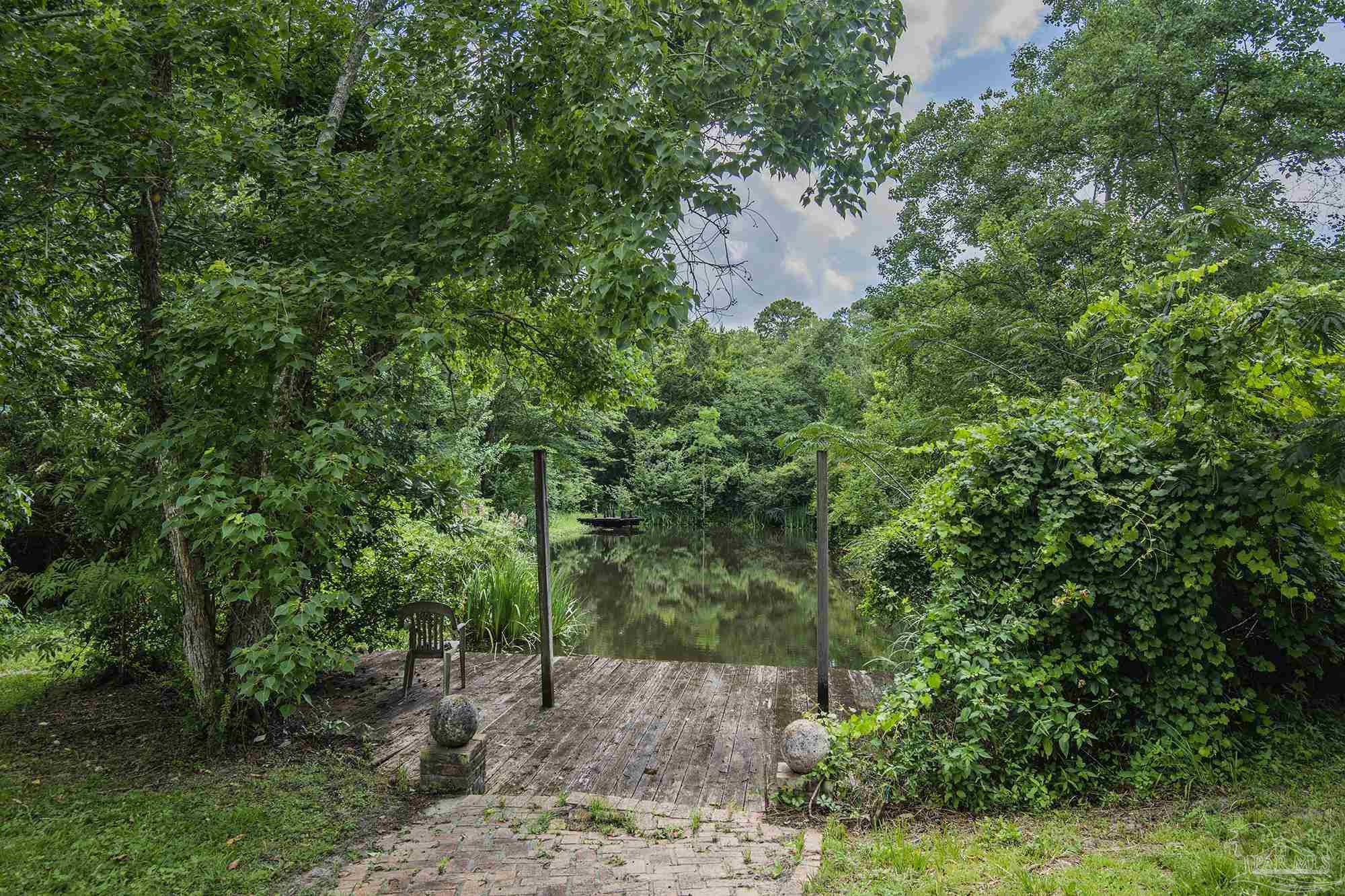 Wooden deck beside a tree-lined pond, with a chair and small dock.