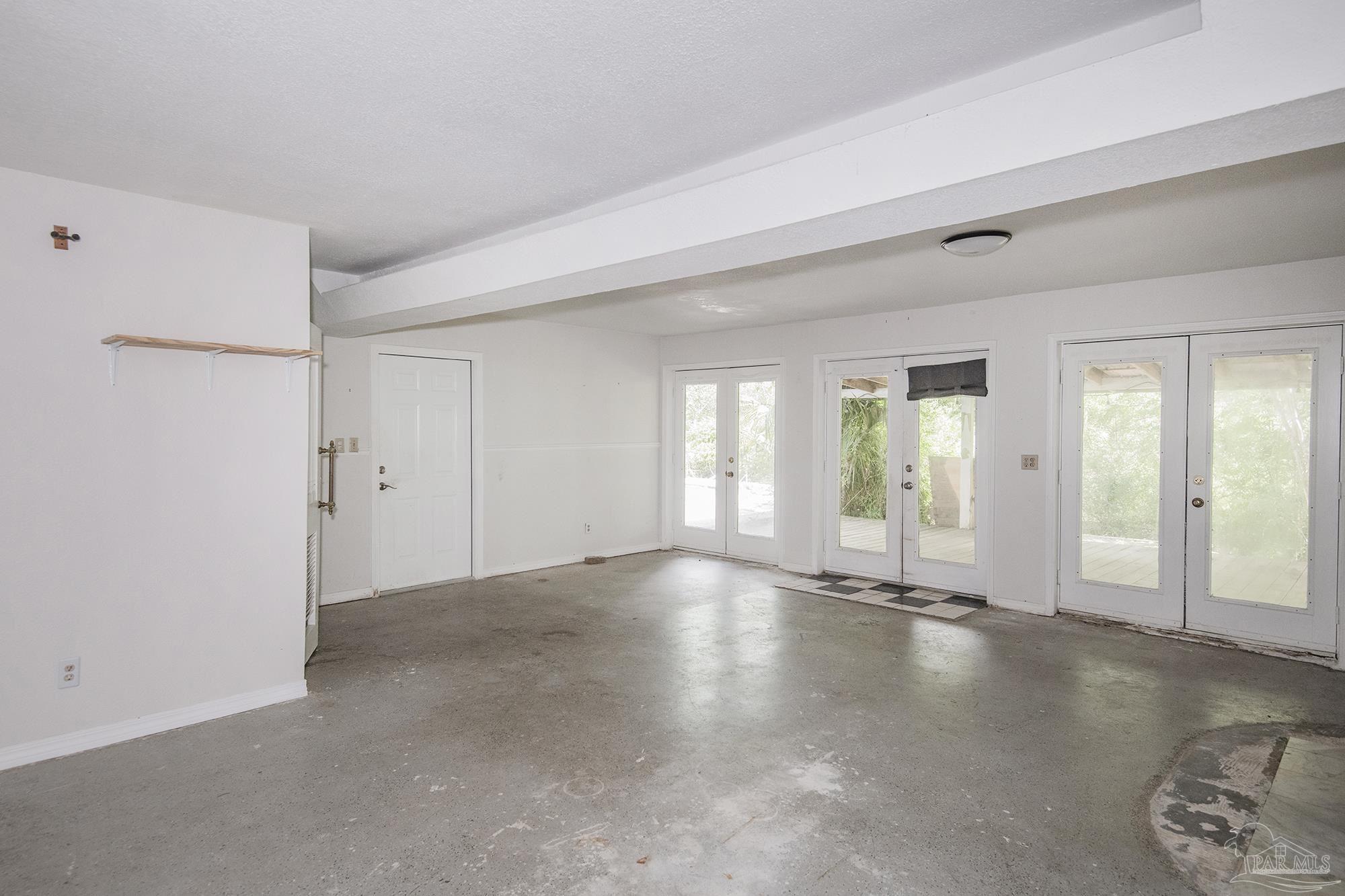 Empty garage with a concrete floor and several glazed doors opening to a deck.