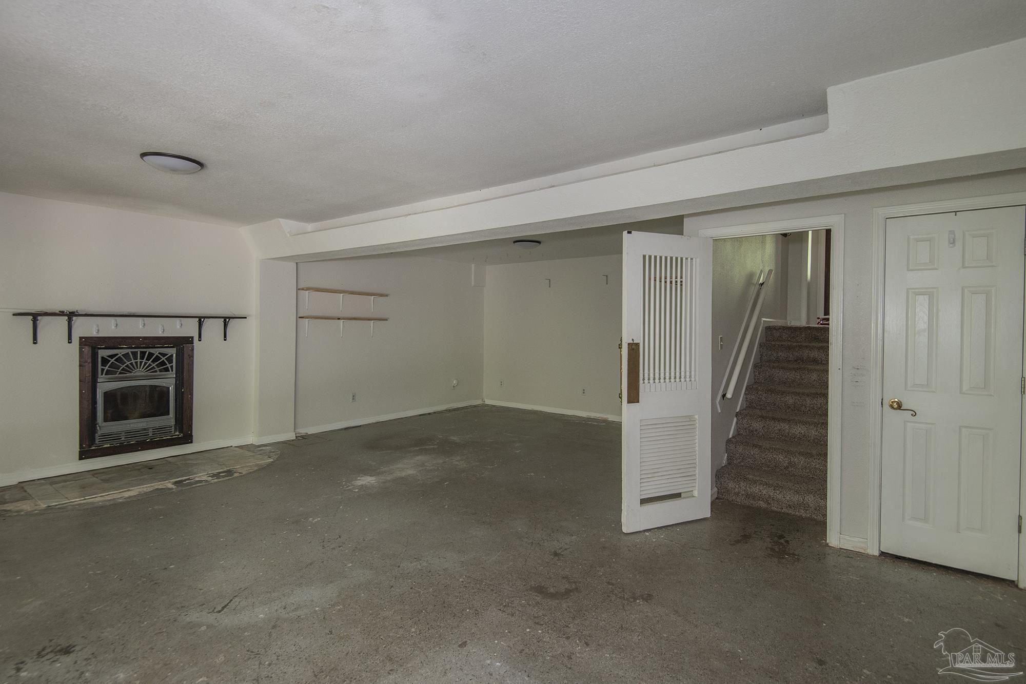 Unfurnished lower-level room with a concrete floor, fireplace, open louvered door, and carpeted stairs.
