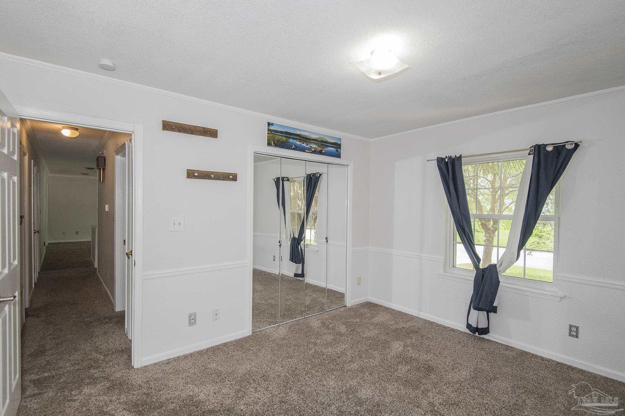 Unfurnished bedroom with mirrored closet doors, brown carpet, and a window with dark curtains.