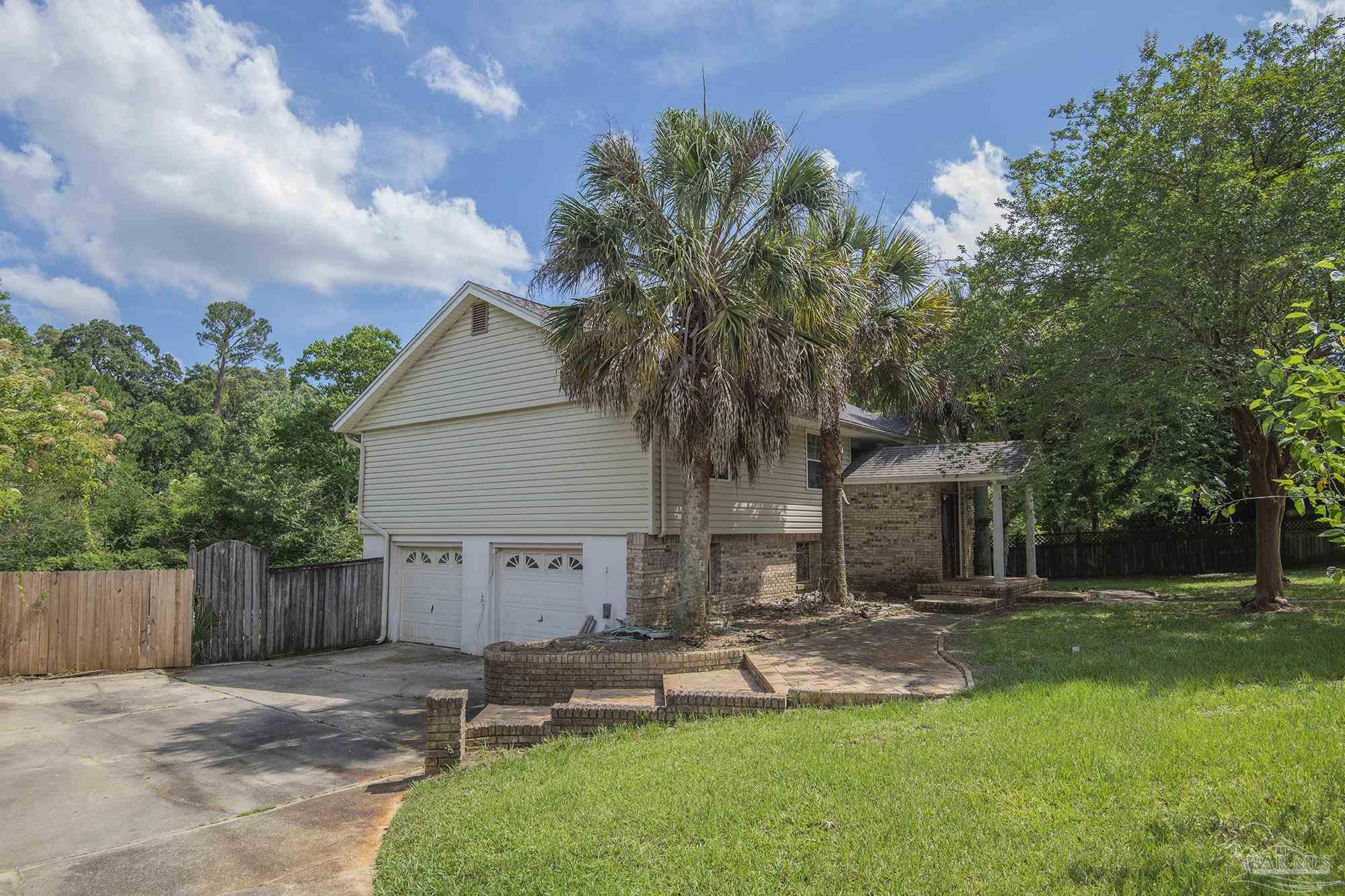 Two-story house with a brick entry, two-car garage, palm trees, and a curved walkway.