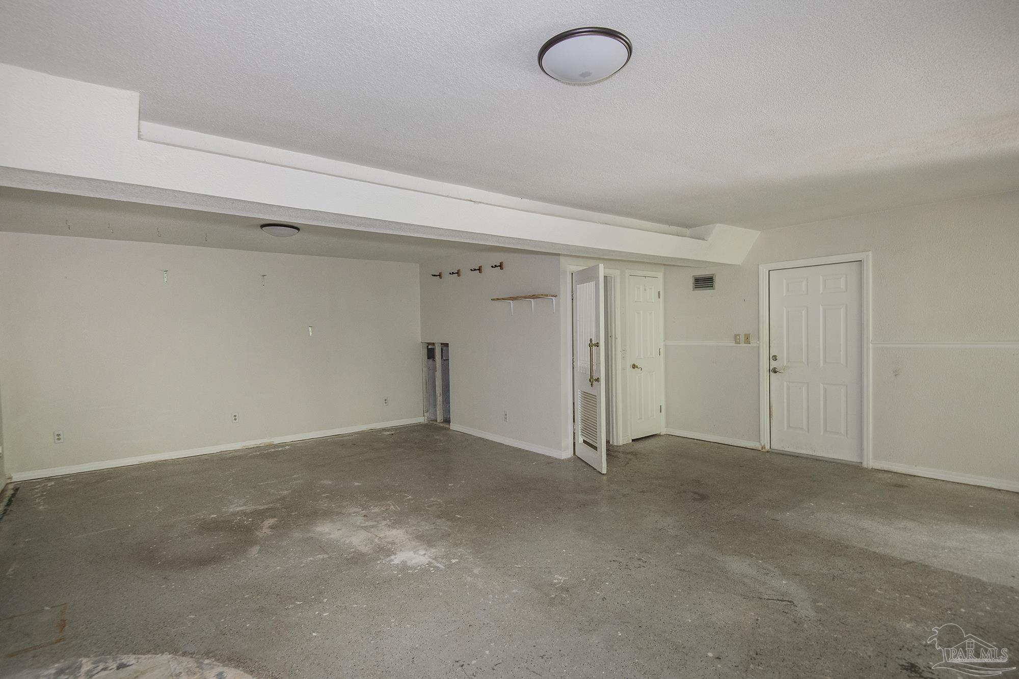 Empty garage with a broad concrete floor, overhead beam, and several doors along the back wall.