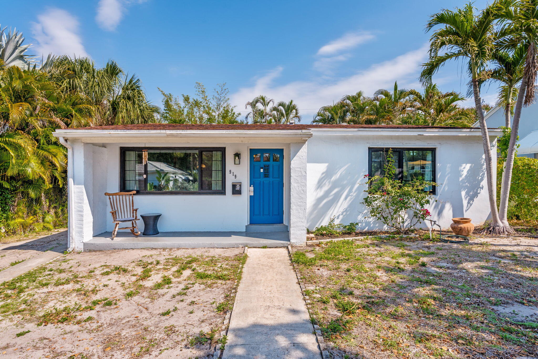White stucco home with a bright blue front door, covered porch, and tall tropical palms.