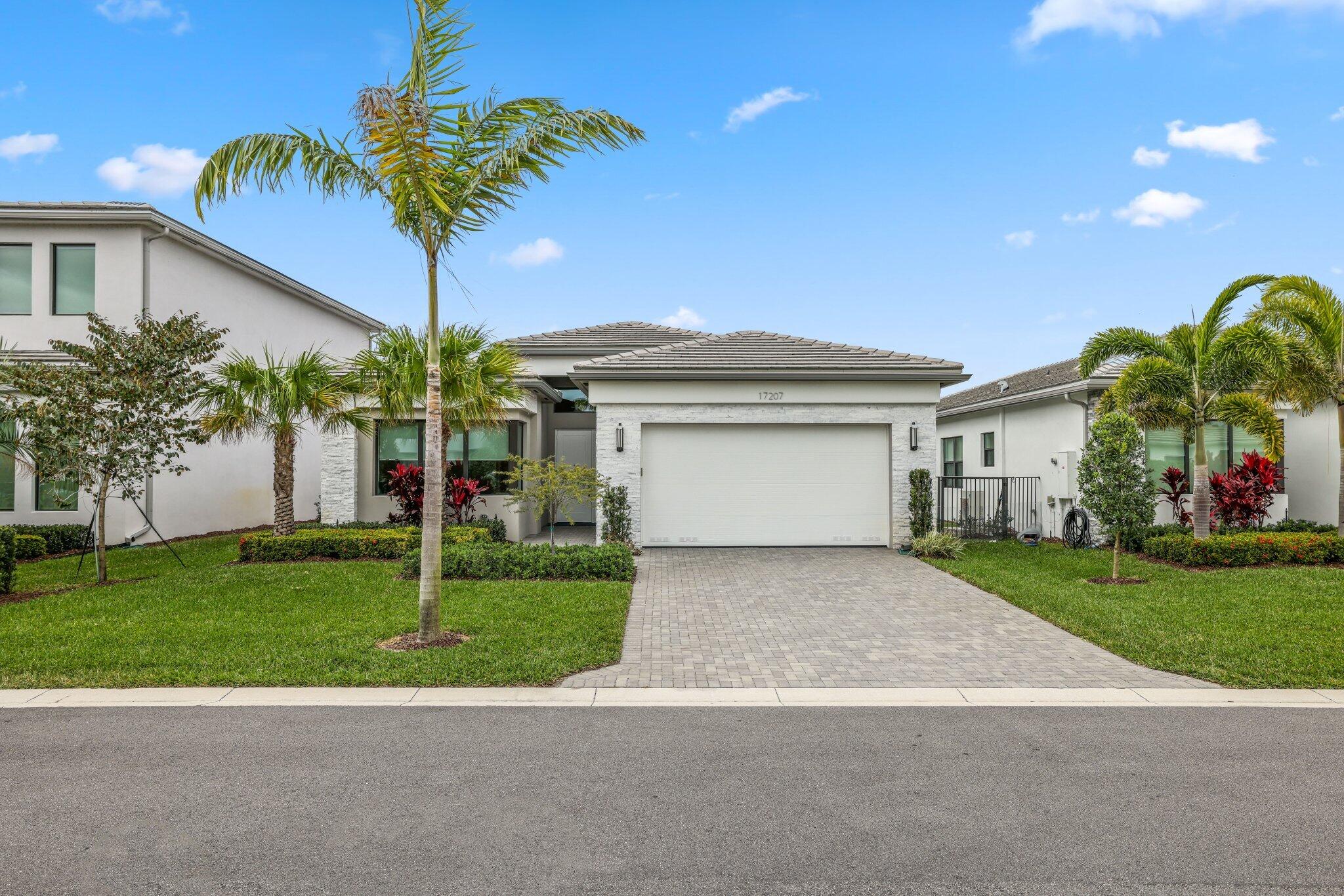 Modern white home with a double garage, paved driveway, and palm trees in the front yard.
