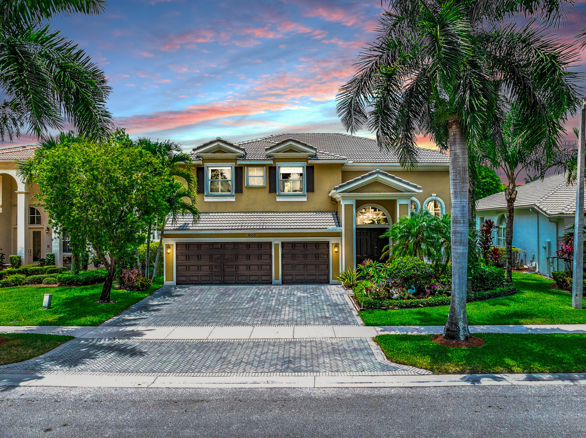 Two-story stucco home with a double garage and palm landscaping under a colorful dusk sky.