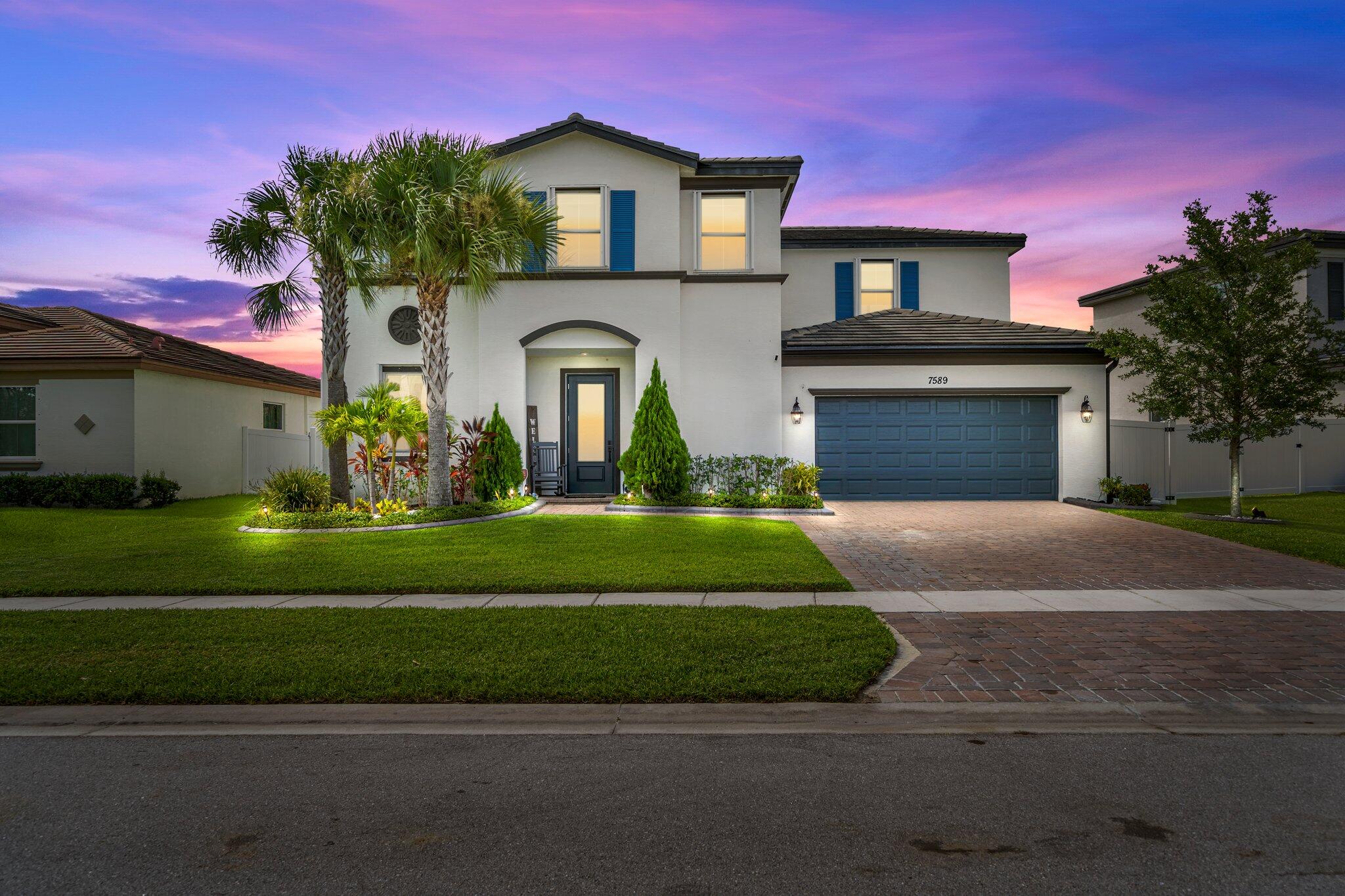 Two-story white stucco home with blue shutters, a blue garage door, and palm trees at dusk.