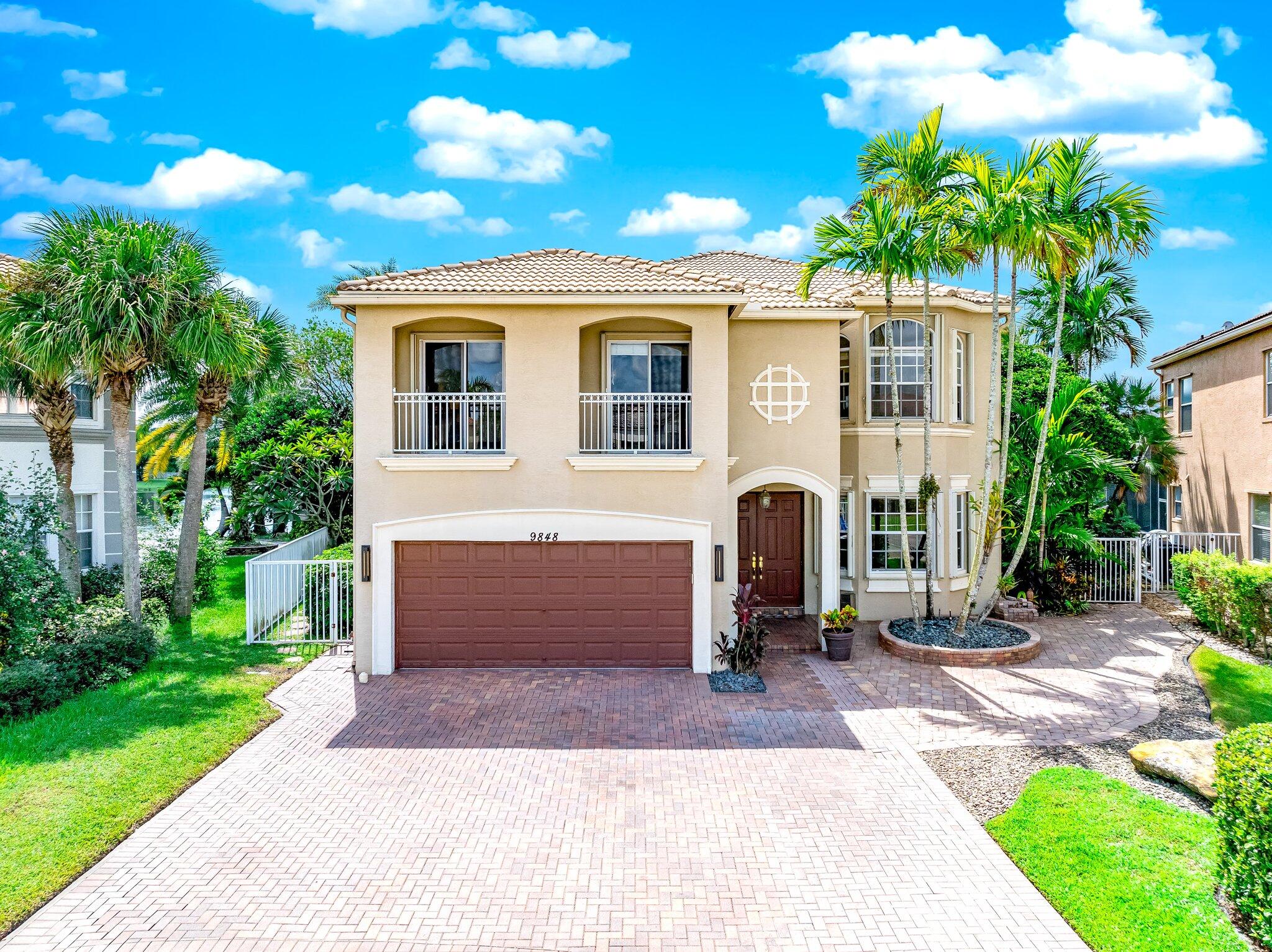 Two-story stucco home with a paver driveway, double garage, and tall palms.