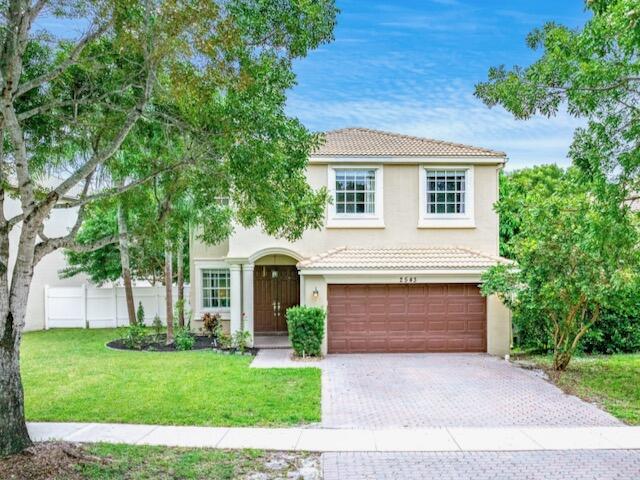 Two-story stucco home with an arched entry, double garage, and mature trees framing the driveway.