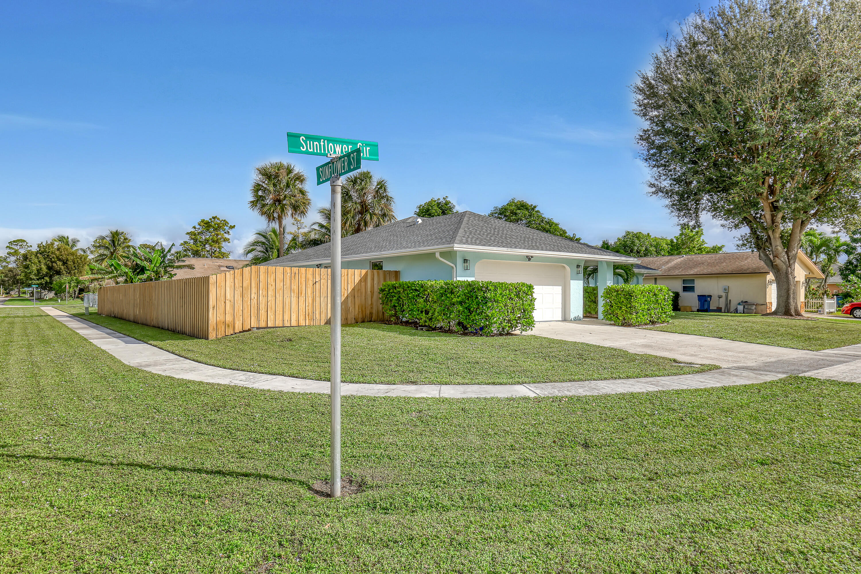 Light blue corner house with a white garage, wooden privacy fence, and Sunflower street signs.