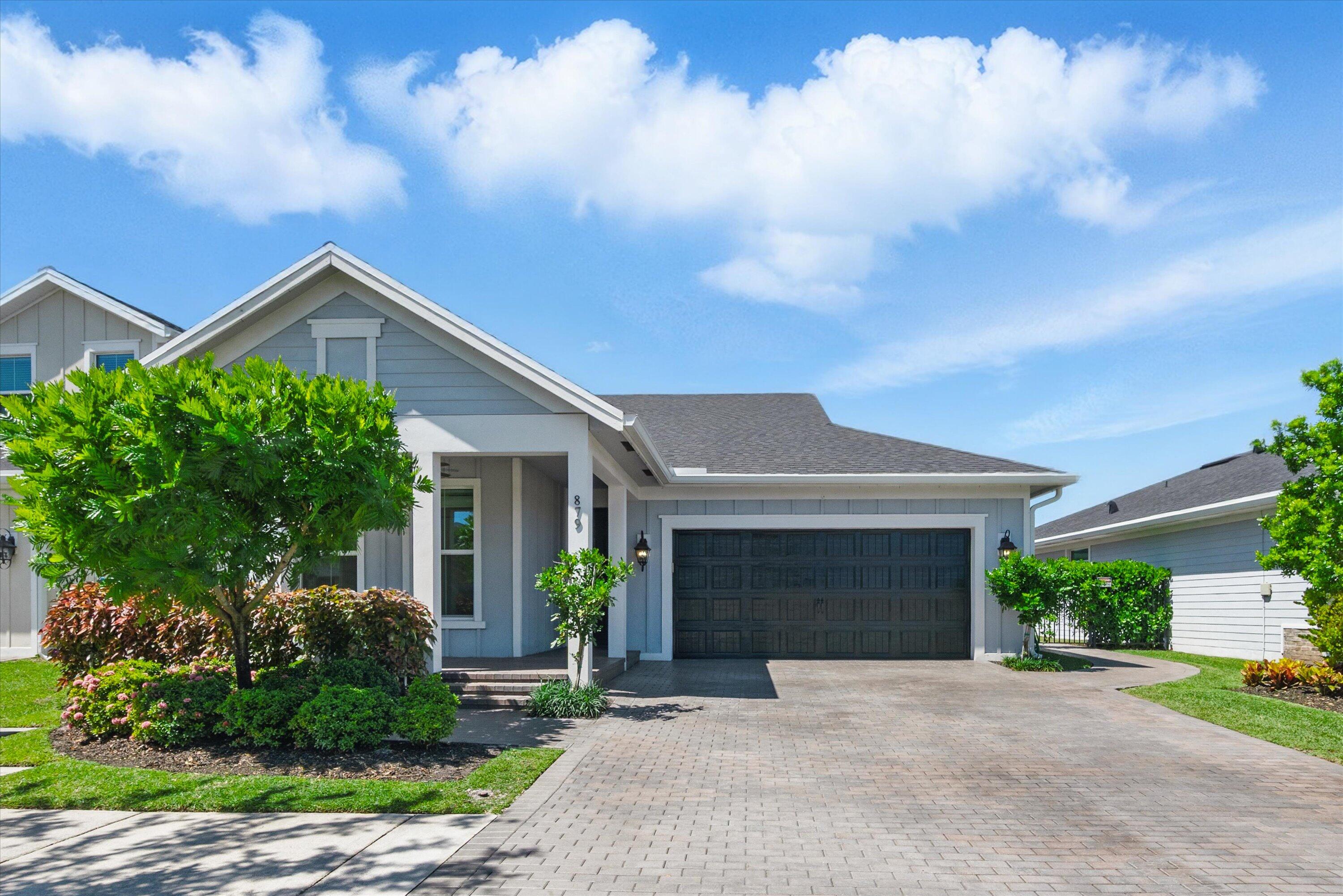 Gray single-story home with a dark attached garage, paver driveway, and landscaped front yard.