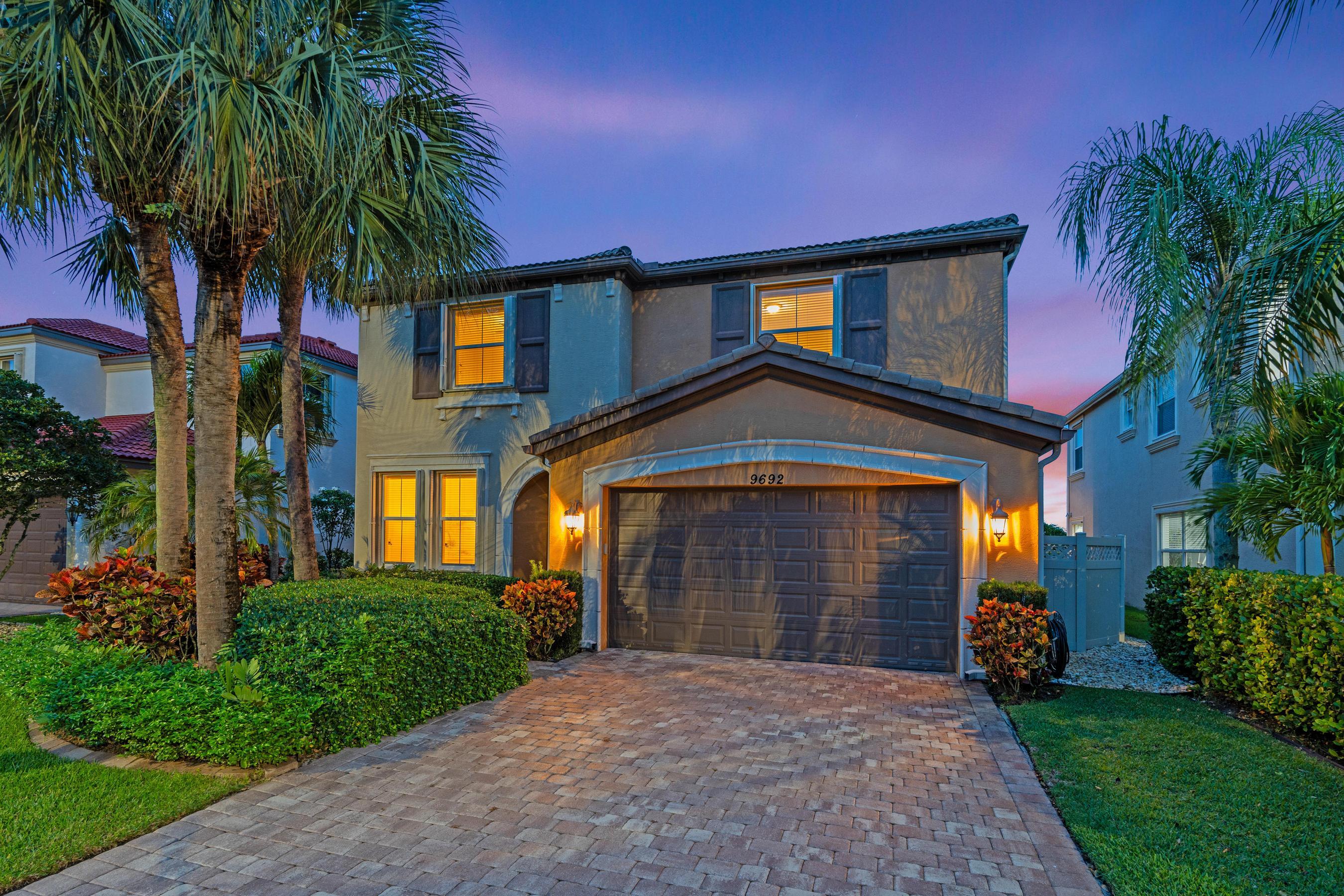 Two-story stucco home with a double garage and palm trees, warmly lit at dusk.