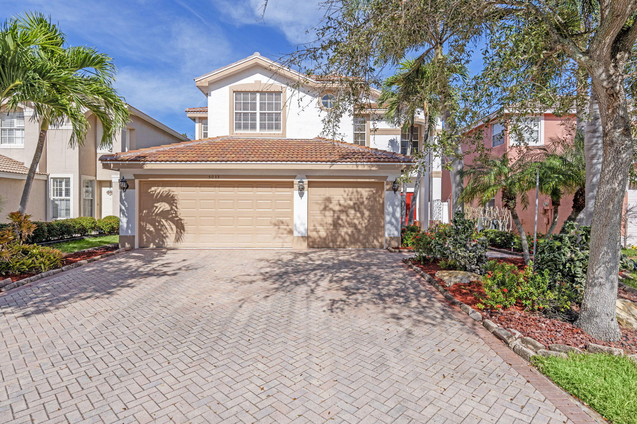 Two-story stucco home with a terracotta roof, double garage, and tropical landscaping.