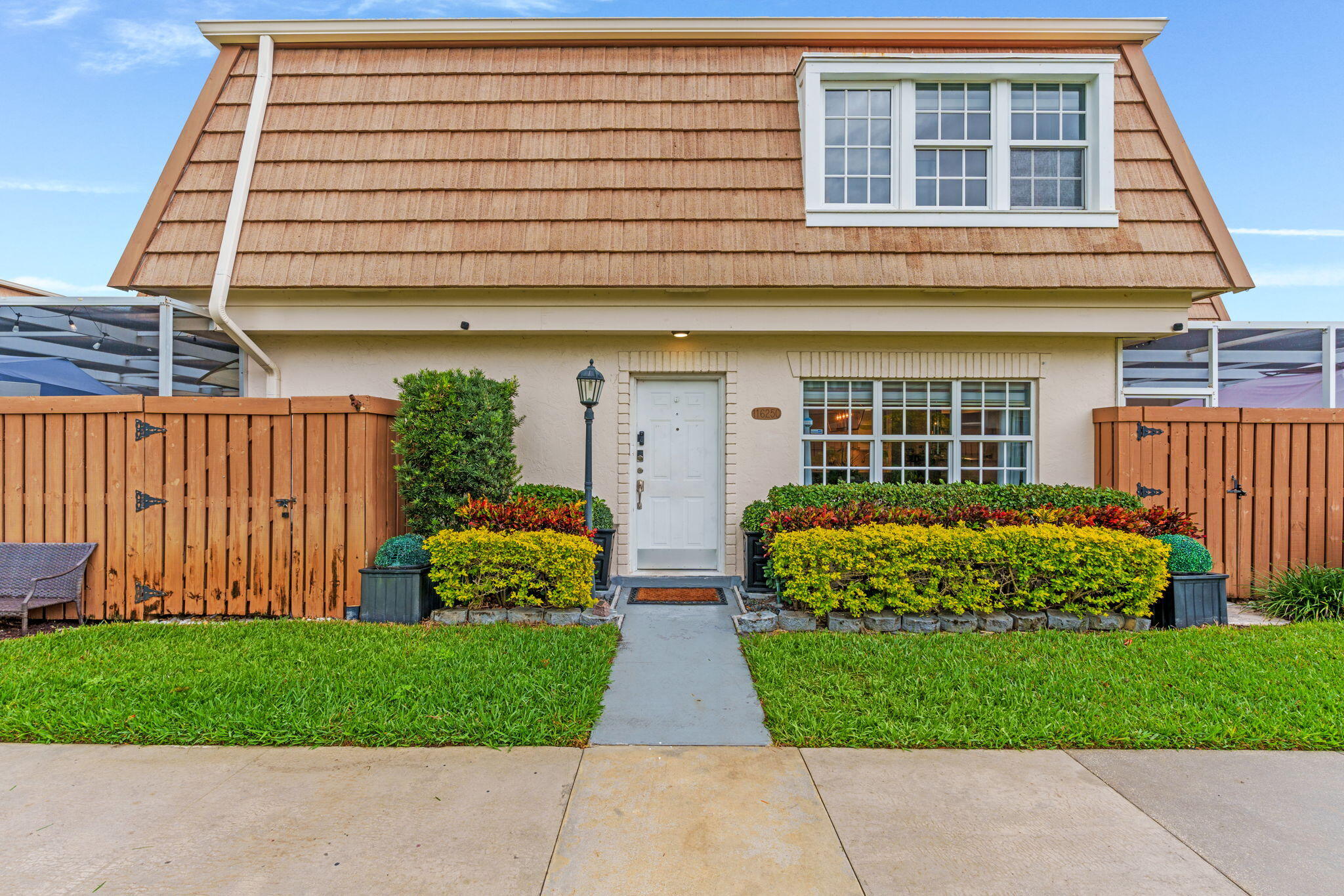 Two-story home with a steep brown roof, wooden privacy fences, and neatly trimmed front hedges.