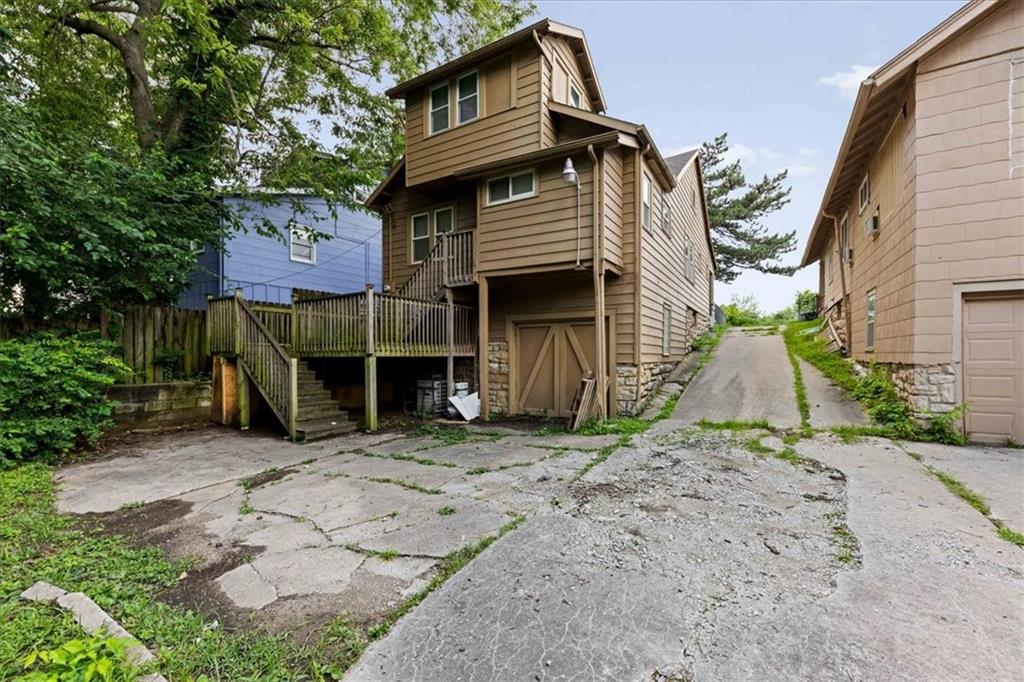 Brown multi-level house with a raised deck and garage beneath it, beside a cracked driveway.