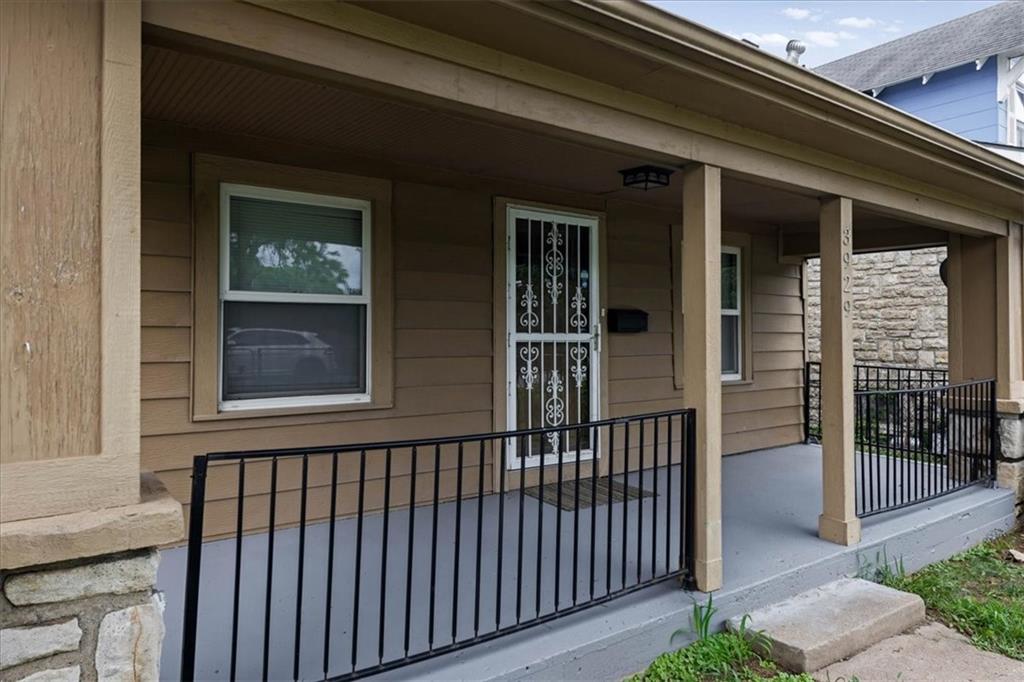 Tan house with a covered porch, black railings, and a decorative white security door.
