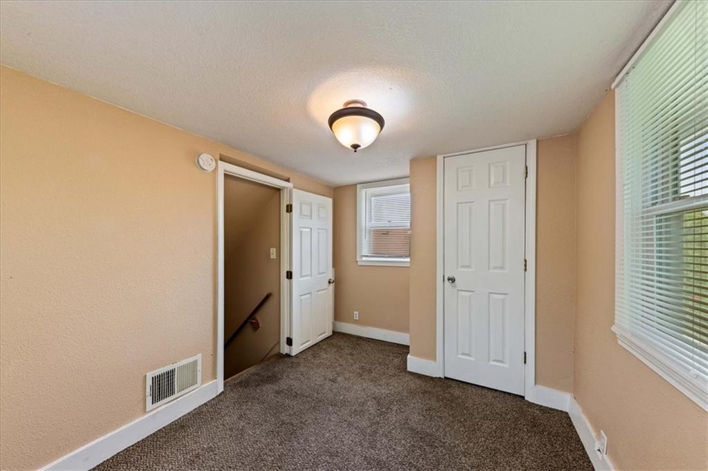 Empty carpeted room with beige walls, two white doors, and windows with blinds.