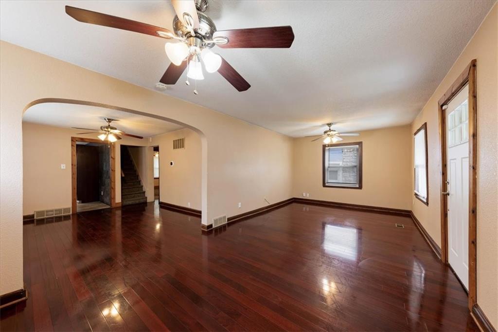 Empty living room with dark hardwood floors, ceiling fans, and an arched opening to the entryway.