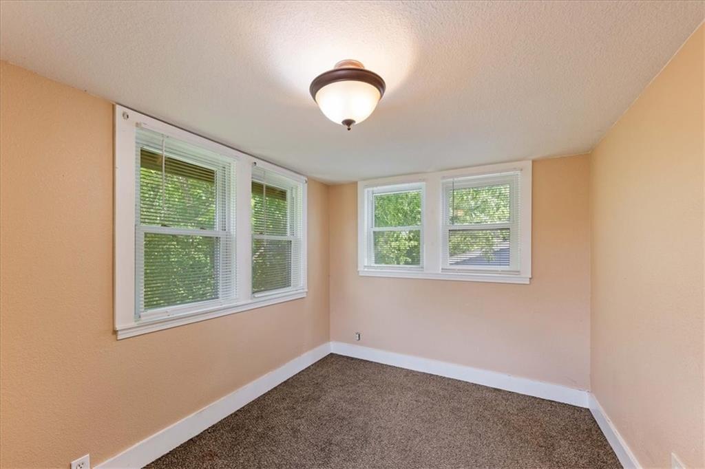 Empty bedroom with peach walls, brown carpet, and multiple windows with blinds.
