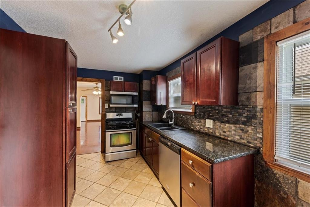 Kitchen with dark wood cabinets, granite counters, stone backsplash, and stainless steel appliances.
