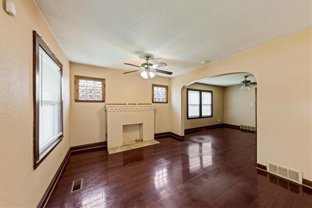 Vacant living room with dark hardwood floors, a tiled fireplace, and an arched opening.