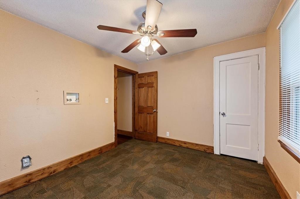 Empty room with patterned carpet, wood trim, ceiling fan, and a window with blinds.