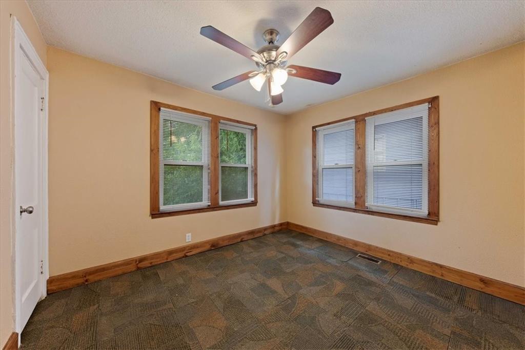 Empty room with patterned carpet, wood-trimmed windows, and a ceiling fan.