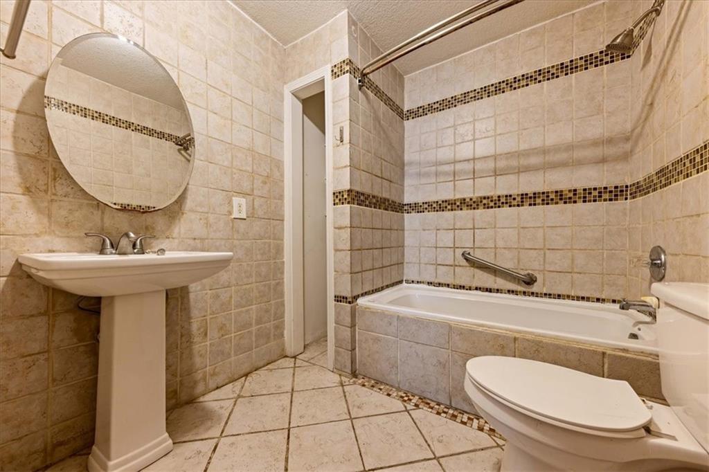Tiled bathroom with a bathtub, pedestal sink, toilet, and round mirror.