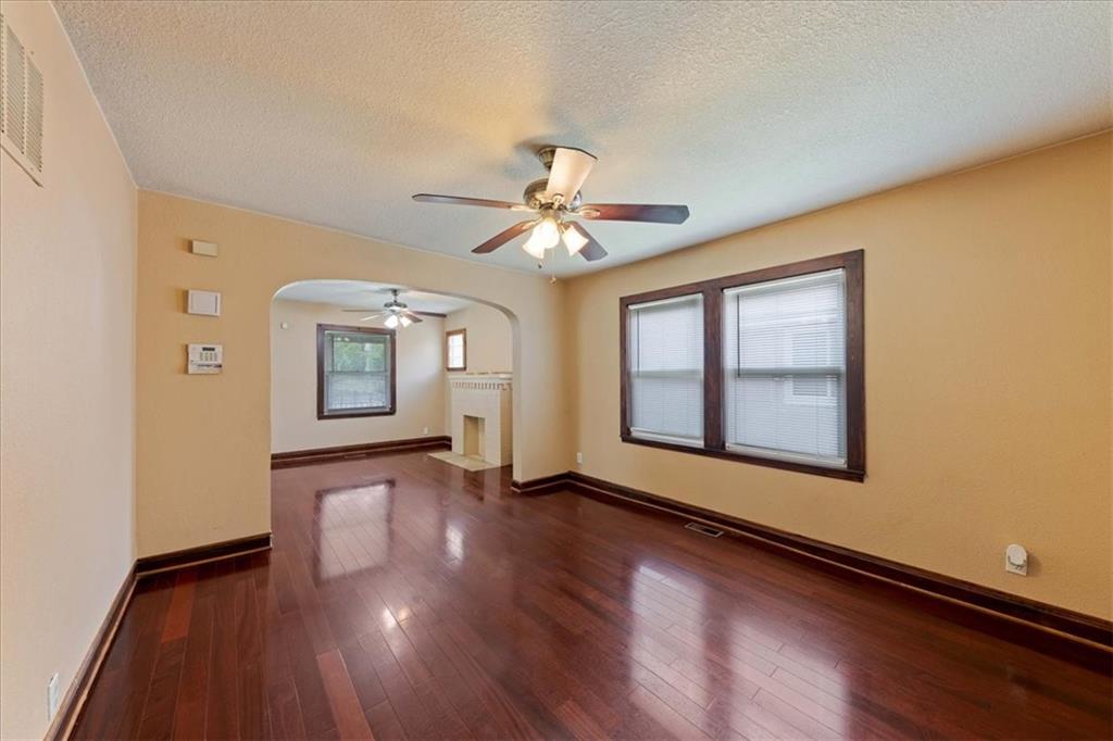 Vacant living room with dark hardwood floors, a ceiling fan, and an arched opening to an adjoining room.