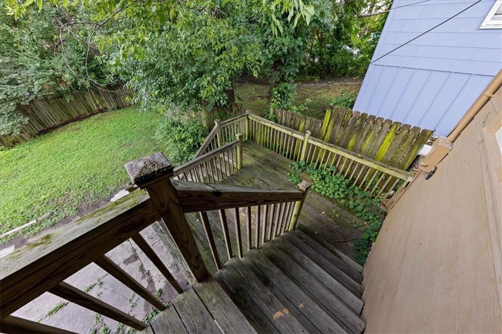 Weathered wooden deck stairs overlook a fenced grassy backyard shaded by mature trees.