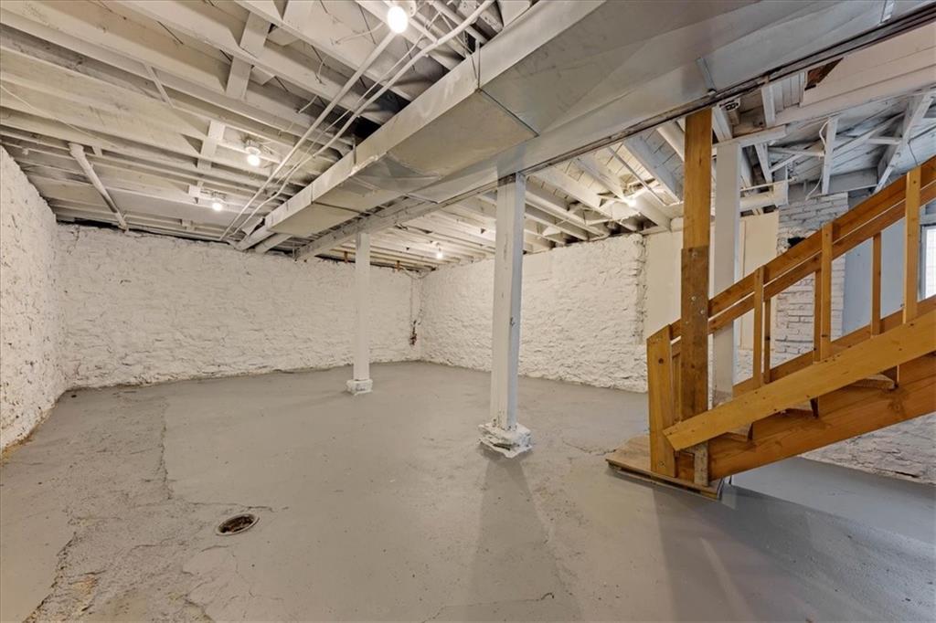Unfinished basement with exposed ceiling beams, concrete floor, and wooden staircase.