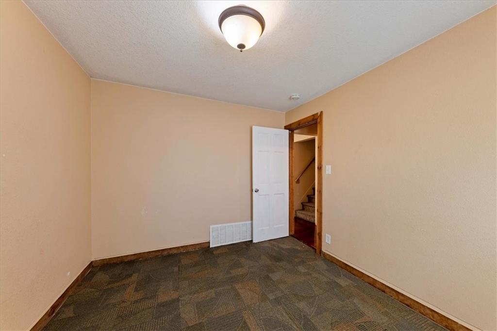 Empty beige room with patterned carpet tiles and an open doorway to a staircase.