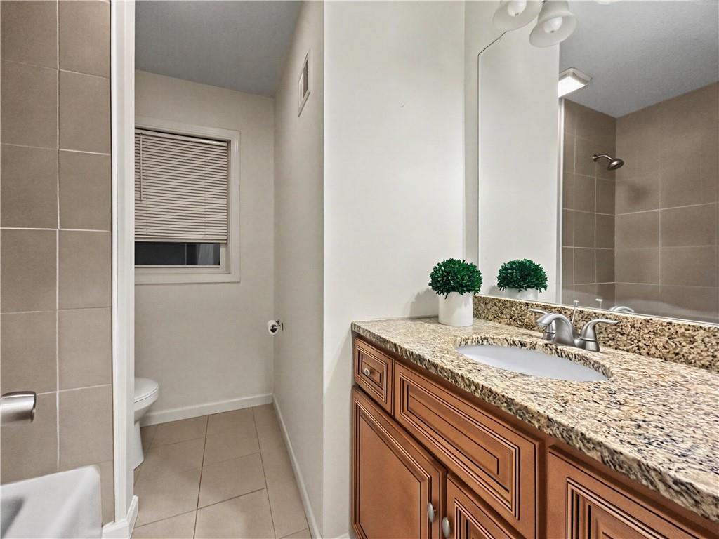 Bathroom with a granite vanity, wood cabinets, large mirror, and separate toilet and tub area.