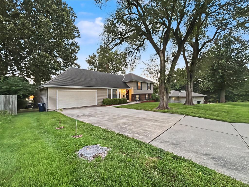 Split-level home with gray siding, a wide garage, and a broad driveway beneath mature trees.