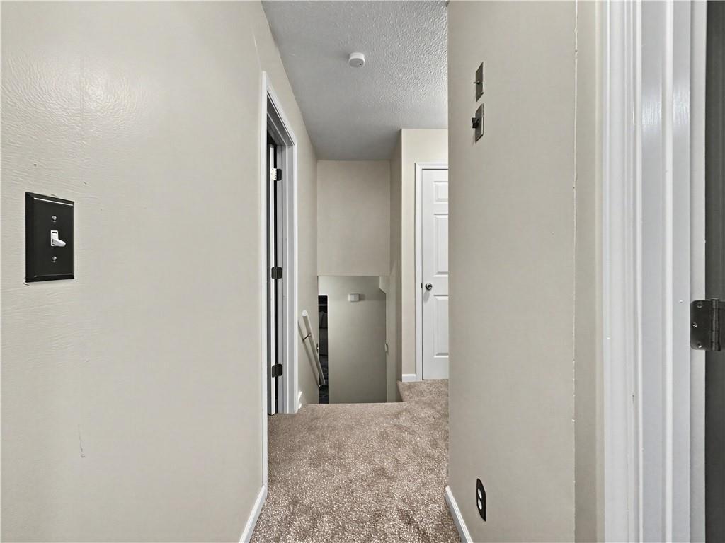 Carpeted upstairs hallway with white walls, doorways, and an opening to the stairs.