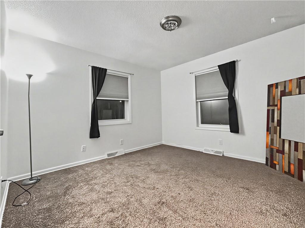 Empty carpeted room with two curtained windows, a floor lamp, and a large framed mirror.