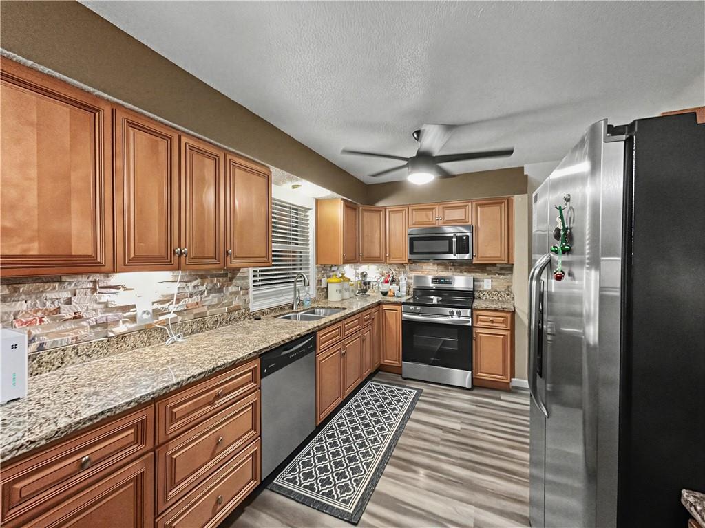 Kitchen with warm wood cabinets, granite counters, stainless steel appliances, and a patterned backsplash.