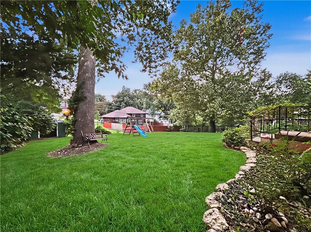 Backyard with mature shade trees, a broad lawn, a children’s play set, and a raised deck.