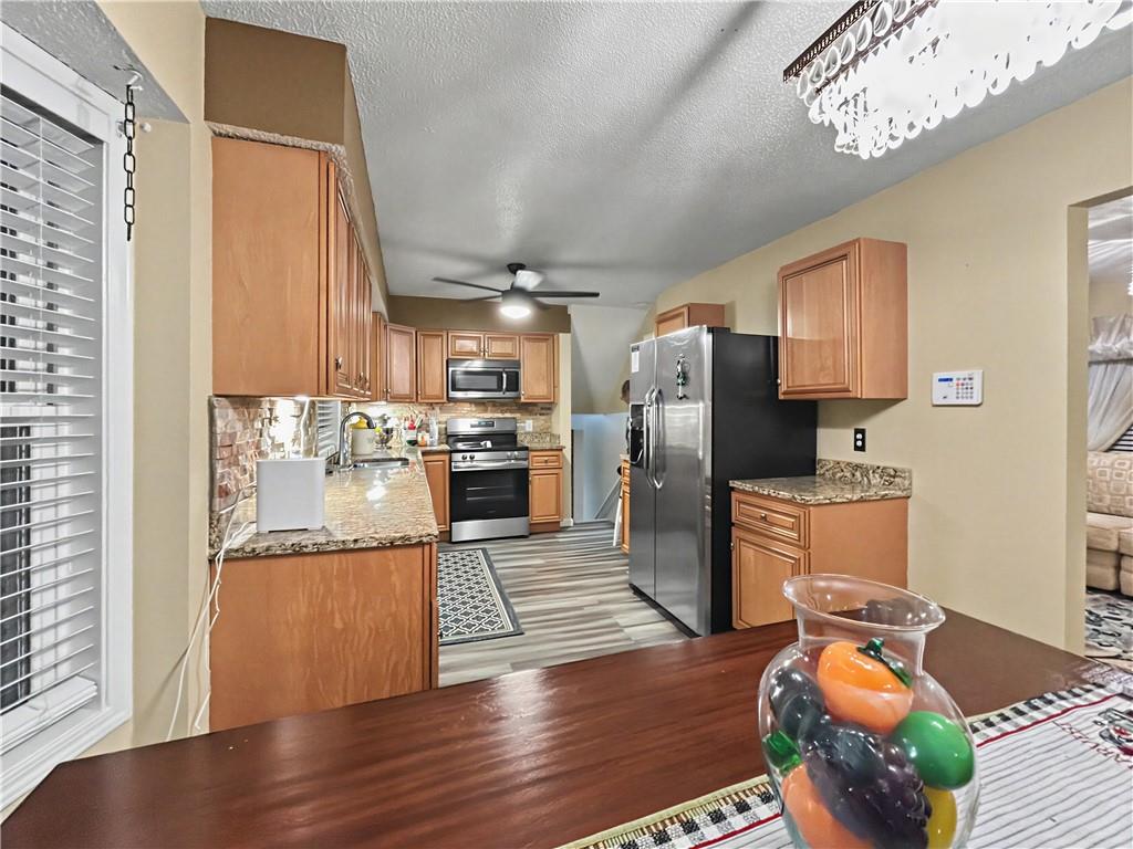 Kitchen with wood cabinets, granite counters, stainless steel appliances, and gray plank flooring.