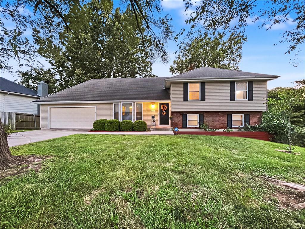 Split-level home with attached garage, brick lower facade, and broad front lawn.