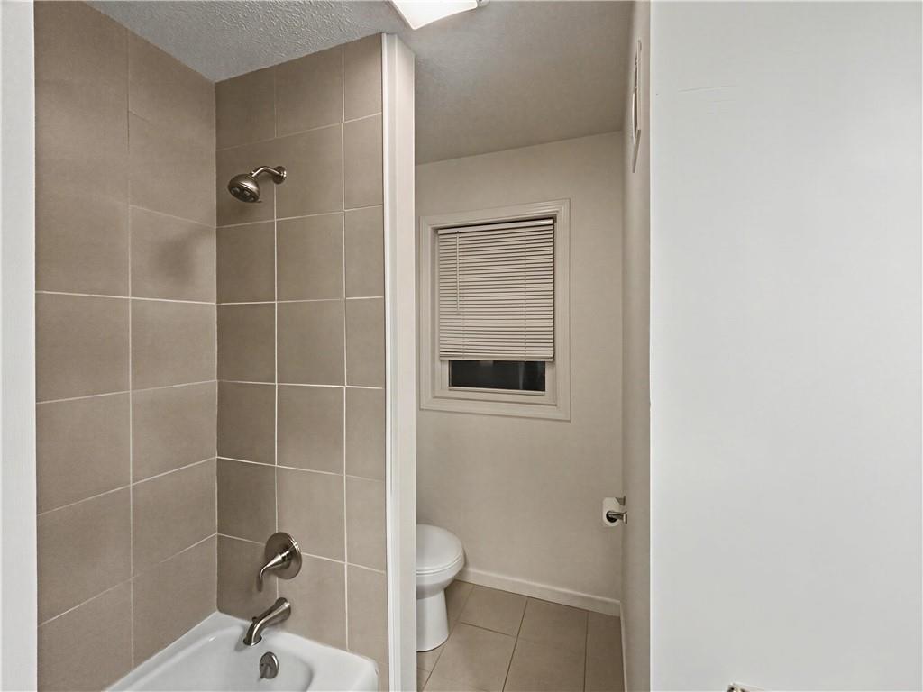 Bathroom with a beige tiled tub and shower, toilet, and small window with closed blinds.