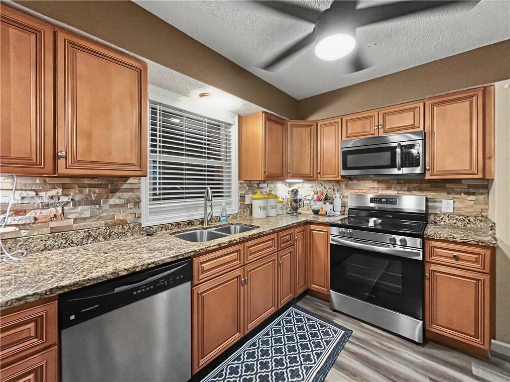 Kitchen with warm wood cabinets, granite counters, stone backsplash, and stainless steel appliances.